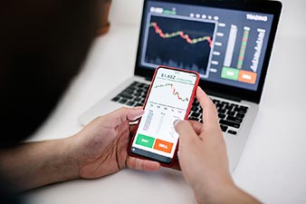 Person trading shares using a laptop and mobile phone