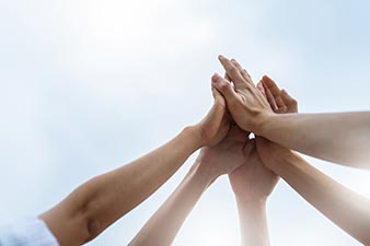 Multiple hands reaching up towards the sky and meeting in a collective high-five