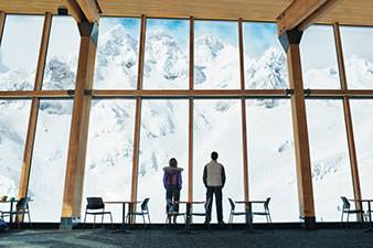 Young couple in front of a large picture window, looking out onto snow-covered mountains