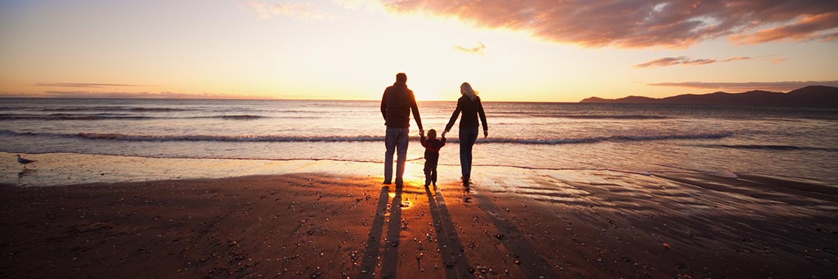 Young parents with small child on the beach at sunset